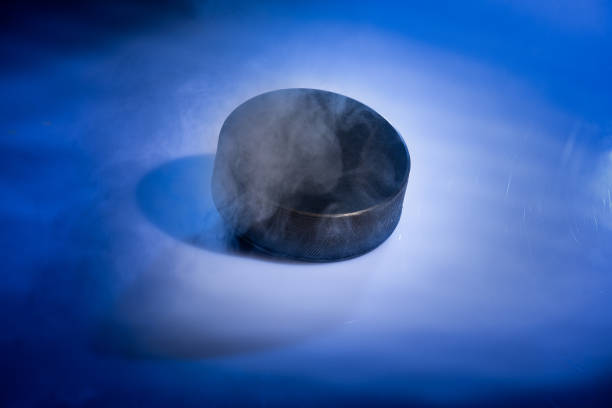 Closeup of a rubbery ice hockey puck against a blue smoky background. stock photo