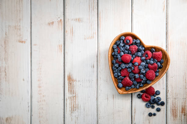 This is an overhead photo of a heart bowl of berries on a white wood background