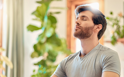 One young caucasian man taking a deep breath in while practising yoga and meditating in harmony at home. Face of a calm, relaxed and focused guy feeling zen while praying quietly for stress relief and peace of mind