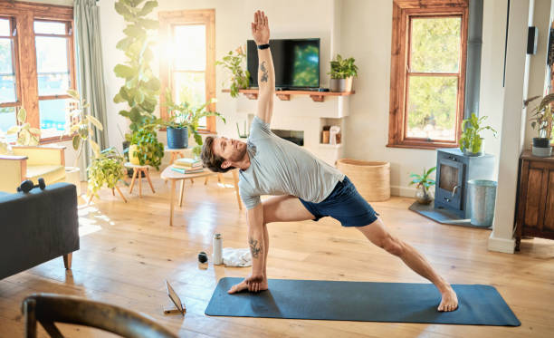 istock One fit young caucasian man doing extended revolved crescent lunge bodyweight exercise with arms outstretched while training with online tutorial on digital tablet at home. Guy gaining muscle, endurance, balance and core strength during yoga workout 1400692966