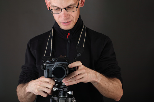 the young man sets a camera on a tripod over a gray background