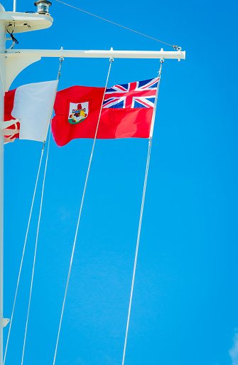 The flag of the island of Bermuda flies in an ocean breeze from the mast of a visiting cruise ship docked in the Royal Naval Dockyard