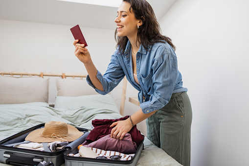 Young woman packing luggage for holiday trip. She is holding her passport.