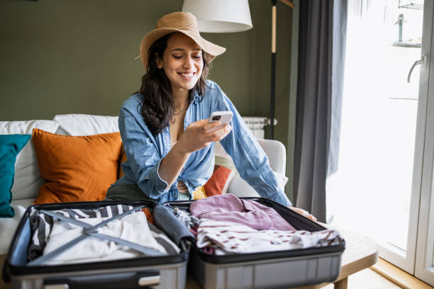 Portrait of woman wearing straw hat and packing for a trip Young woman sitting on the couch, packing suitcase and texting one young woman only stock pictures, royalty-free photos & images