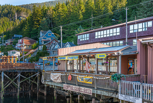 Ketchikan, Alaska, USA - July 17, 2011: Retail businesses built on wharf along Water Street featuring coffee shop, fishing charters, snacks, laundry services, and more. Green forest in back.