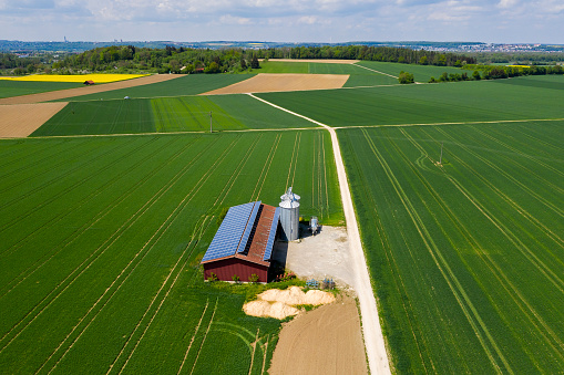 Agricultural building with solar panels and silos between green fields, viewed from above.