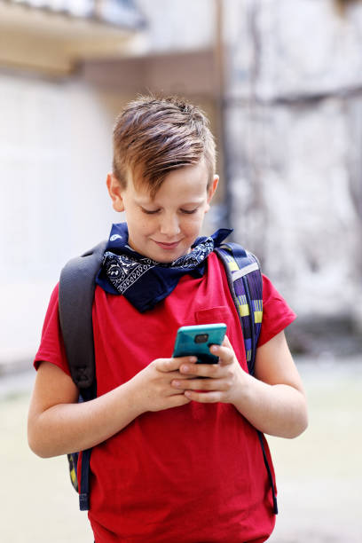 istock Cute little boy typing a message or browsing social media on his smart phone, carrying a schoolbag, going home from school 1400707609