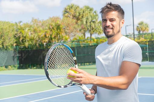 Portrait of a male player with racket and ball near the net at tennis court