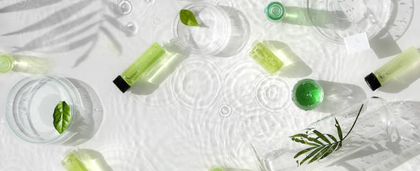 Cosmetic skincare background. Herbal medicine with green leaves. Natural sunlight, long shadows. Splashes of water, splashes. Chemical glassware, petri dishes, vials. Natural body care concept. stock photo