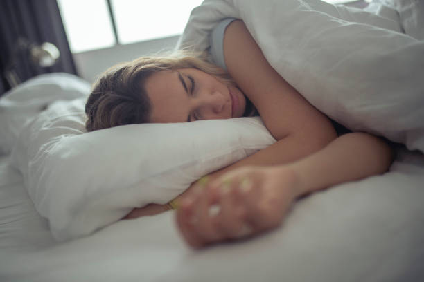 une belle femme dort sur les draps blancs d’une chambre d’hôtel. - pillow wake up yawning sleeping photos et images de collection