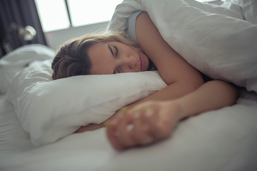 A millennial woman sleeps on a comfortable hotel room bed.