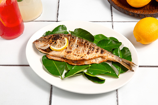 Baked fish meat with lemon and leaves on white plate