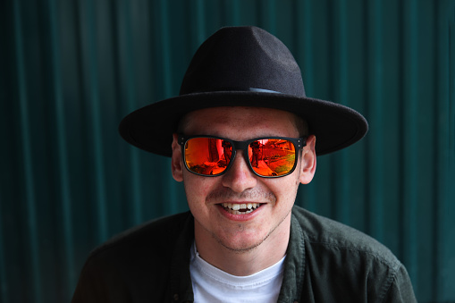 Smiling fashion man. Portrait of handsome smiling stylish hipster lambersexual model. Man dressed in red polarization sunglasses. Fashion male on the modern blue background.