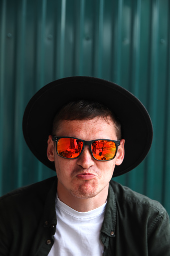 Funny man. Smiling fashion man. Portrait of handsome smiling stylish hipster lambersexual model. Man dressed in red polarization sunglasses and hat. Fashion male on the modern background.