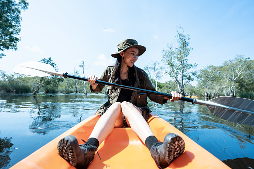 Asian young attractive tourist woman rowing kayak alone in forest lake. Backpacker traveler girl travelling and kayaking on canoe in beautiful mangrove forest enjoy spend time on holiday vacation trip