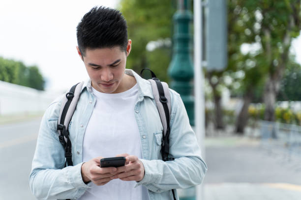 istock Asian attractive male backpacker chatting on mobile phone walk in city. Active handsome man tourist traveler travel alone on street use smartphone enjoy spend time on holiday vacation trip in Thailand 1400714981