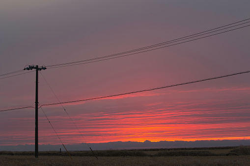A single utility pole silhouetted against a red, stripy sunset