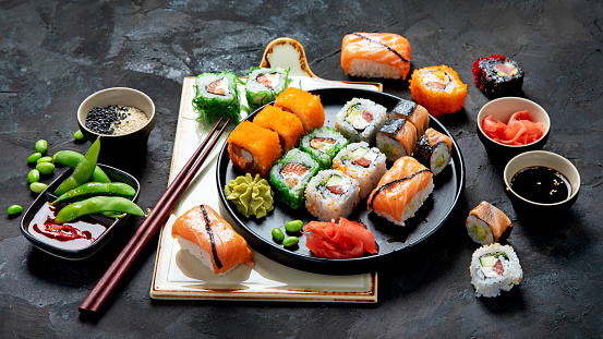 Sushi take-out containing a selection of salmon sushi specialities and sauces in a polystyrene tray with chopsticks on the side.