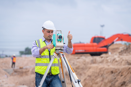 Surveyor engineers wearing safety uniform ,helmet and radio communication with equipment theodolite to measurement positioning on the construction site of the road with construct machinery background