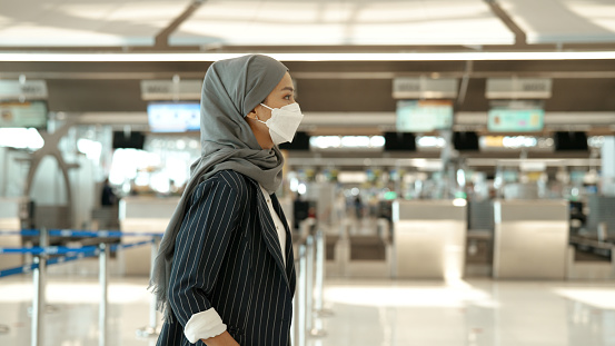 An Asian muslim woman in face mask heading for the waiting area after finishing her check-in process.