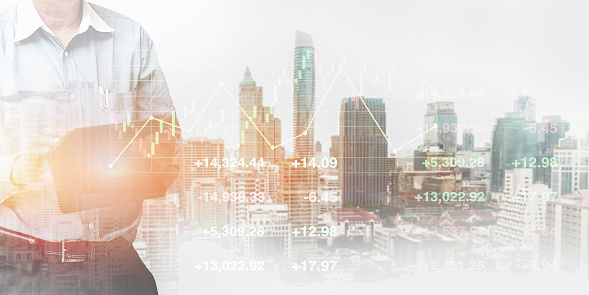 Businessman  standing and operate tablet to control stock financial index data on blurry urban real estate background with graph and chart.Double exposure  background for business presentation.
