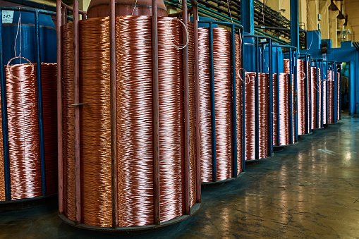 Coiling shiny red copper cable onto huge reels to package on floor in spacious workshop of contemporary production plant