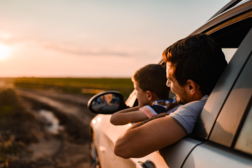 Beautiful father and son enjoying on a road trip on sunset.