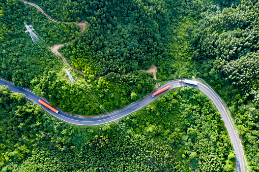 Aerial view of long vehicle truck with special semi-trailer for transporting oversized load or exceptional convoy through a rural forest and mountainous area. Transportation and industrial concept to support economic growth