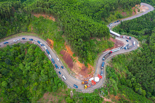 Aerial view of long vehicle truck with special semi-trailer for transporting oversized load or exceptional convoy through a rural forest and mountainous area. Transportation and industrial concept to support economic growth