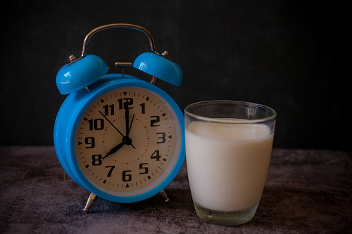 Close up a glass of milk and blue vintage alarm clock. 20.00 o'clock late evening and time to go to bed. Healthy sleep, sweet dreams concept. 8.00 o'clock morning time for breakfast concept.