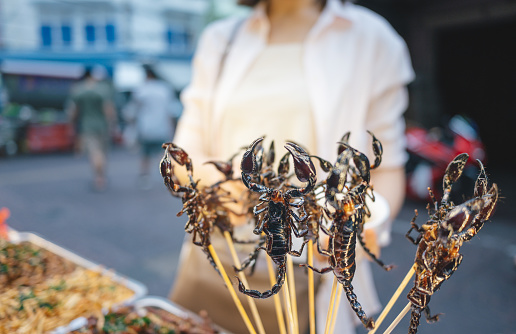 Young asian local people wear facemask buy fired insects in yaowarat local street food marketplace in Bangkok thailand