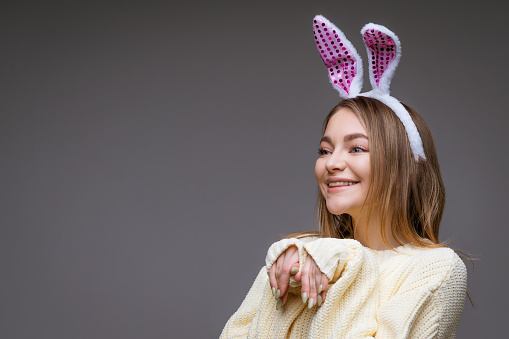 portrait of caucasian cute girl with bunny ears on gray background, cheeky bunny concept