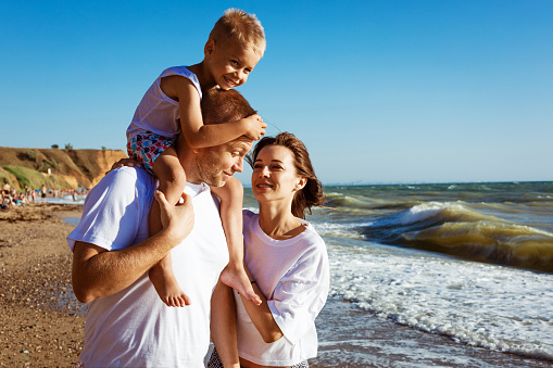 Happy family having fun on summer vacation. The son is sitting on the daddy's neck. Young family on vacation have a lot of fun together.