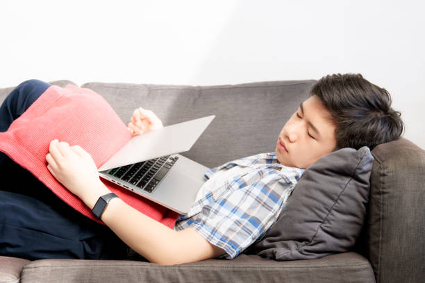 Tired handsome Asian teenage boy lying, sleeping on sofa with half closed laptop computer on him while study online lessons at home Tired handsome Asian teenage boy lying, sleeping on sofa with half closed laptop computer on him while study online lessons at home boring homework twelve stock pictures, royalty-free photos & images