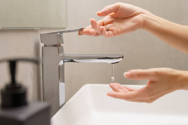 nahaufnahme der hand der frau, die am wasserhahn mit einem wassertropfen in die hand tropft - faucet water drop house stock-fotos und bilder
