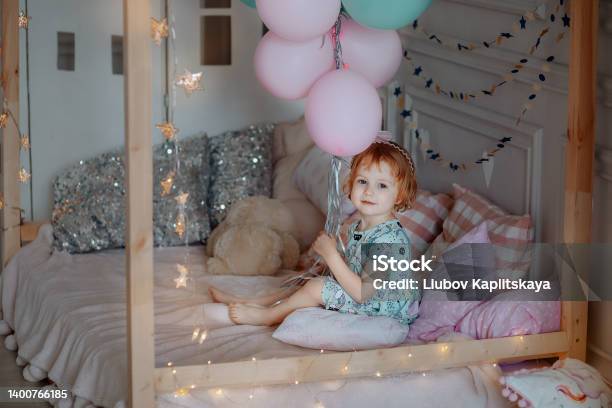 Little Baby Girl In A Blue Dress Is Sitting On The Bed Stock Photo - Download Image Now