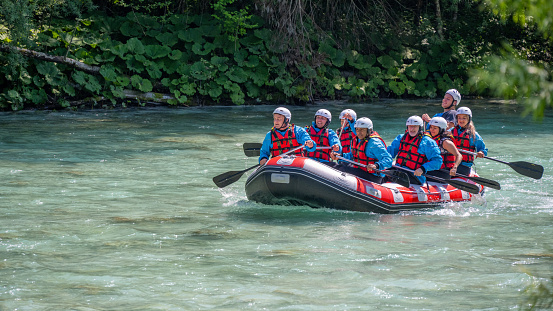 Team of whitewater rafters rowing their raft across the rapids in river.