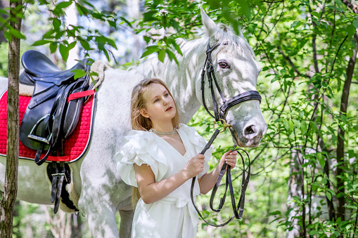 A teenage girl with her favorite white horse for a walk in the spring forest. Communication with animals in nature. Horizontal photographs of animals and people.