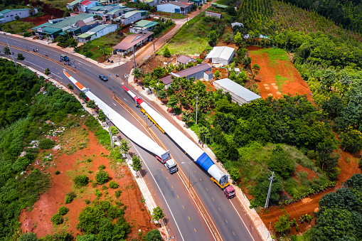 Aerial view of long vehicle truck with special semi-trailer for transporting oversized load or exceptional convoy through a rural forest and mountainous area. Transportation and logistics concept for economic growth