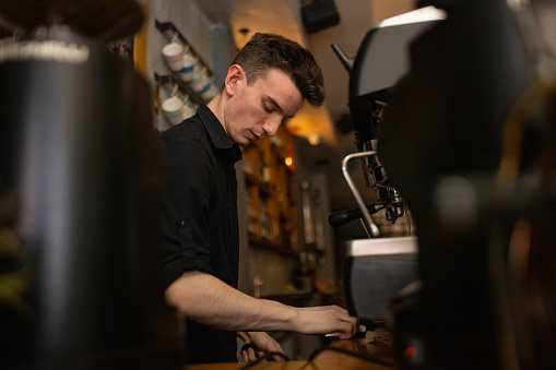 Caucasian male barista making coffee while using espresso maker, at the coffee shop