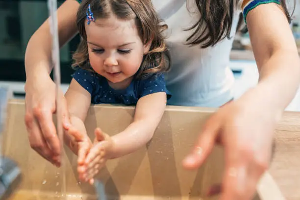 Young mother helping her toddler girl wash her hands