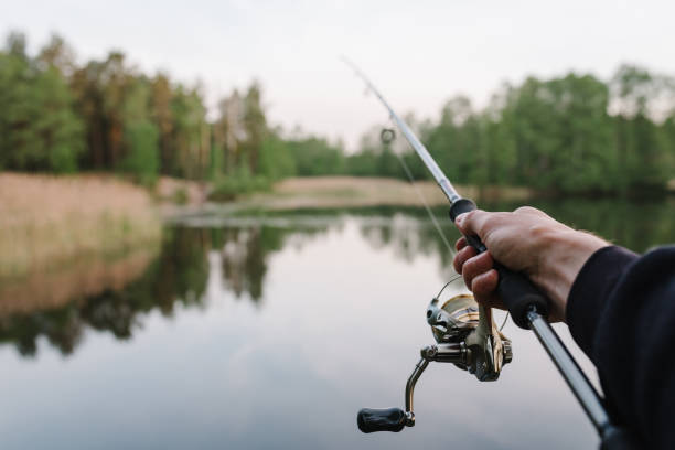 istock Fisherman with rod, spinning reel on the river bank. Man catching fish, pulling rod while fishing from lake or pond with text space. Fishing for pike, perch on beach lake or pond. Fishing day concept. 1400775000