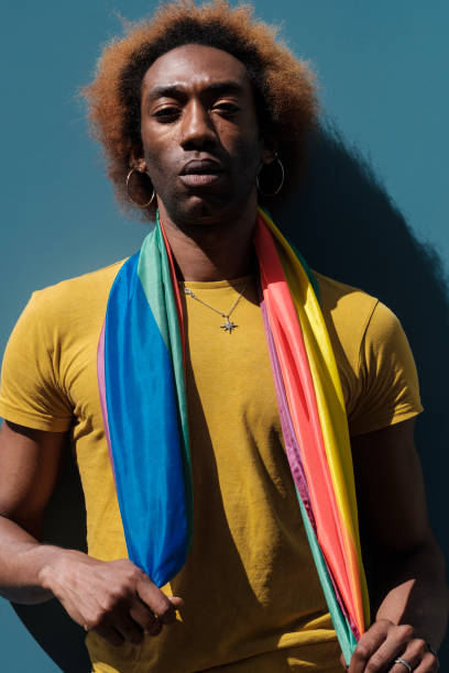 istock Portrait of non-binary young person looking at camera leaning against a blue wall. Lgbtq flag. 1400776692