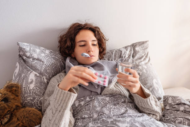 Health condition disease of young lady teenage girl has cold, lies in bed covered with blanket, with electronic thermometer, glass of water and blister of antipyretic pills. Viral infection, fever, colds, malaise, flu, runny nose, cough cough lozenge stock pictures, royalty-free photos & images