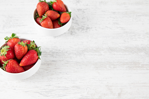 Fresh ripe strawberries in a white bowl on a white wooden background