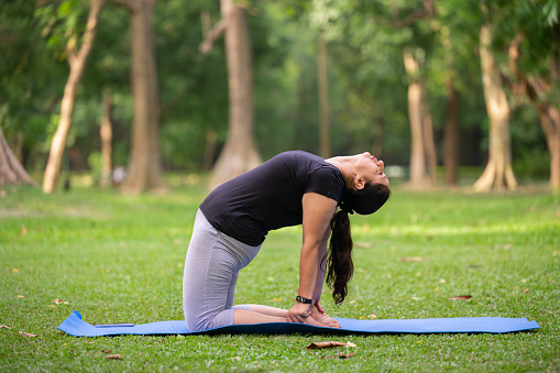 Outdoor image of active senior woman doing camel pose or Ustrasana exercise at park
