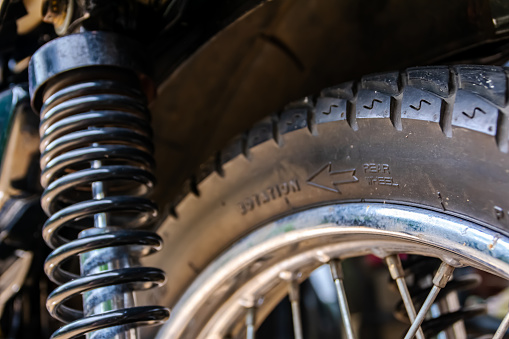 Back side of vintage motorcycle showing metallic steel spoke wheels with a black rubber tire and the spring of shock absorber at the side. Suitable for auto garage and race team wallpaper