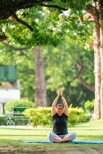 Outdoor image of healthy woman sitting in Namaste or prayer yoga position and relaxing at park