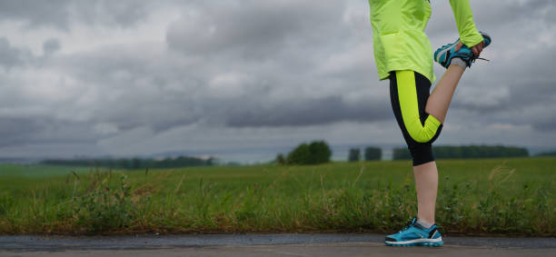 Fitness runner stretching before run of the road. Healthy young woman warming up outdoors.
