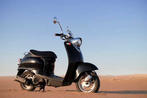 Walvis Bay, Namibia -28 May, 2022: The Retro black scooter at sunset in the golden sand of the Namib Desert